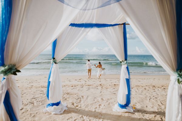 Decoración boda en la playa; imagen de unos novios a punto de casarse donde se ve en el fondo la arena y el mar